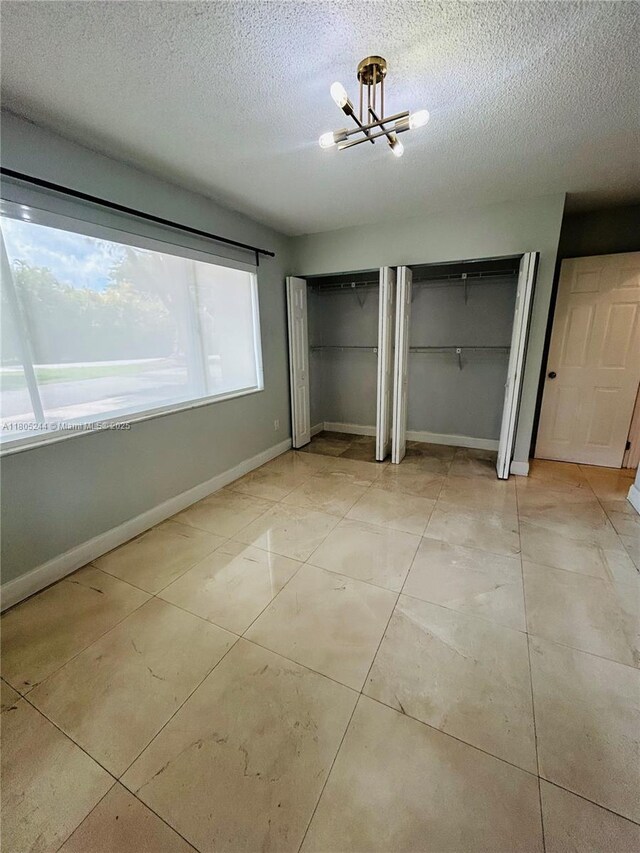 3480 Torremolinos Ave Unit A-33, Doral, FL 33178 - unfurnished bedroom featuring two closets, a chandelier, a textured ceiling, baseboards, and light tile patterned flooring
