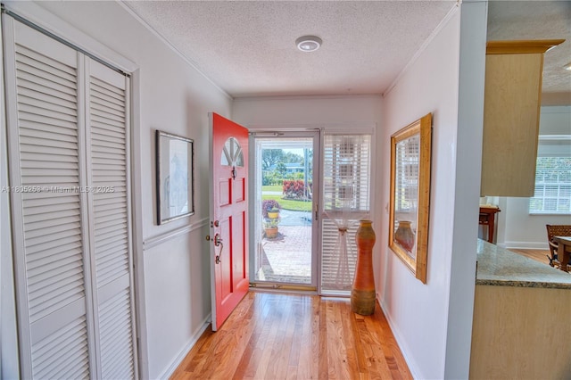 foyer entrance featuring a textured ceiling, light wood-type flooring, ornamental molding, healthy amount of natural light, and baseboards