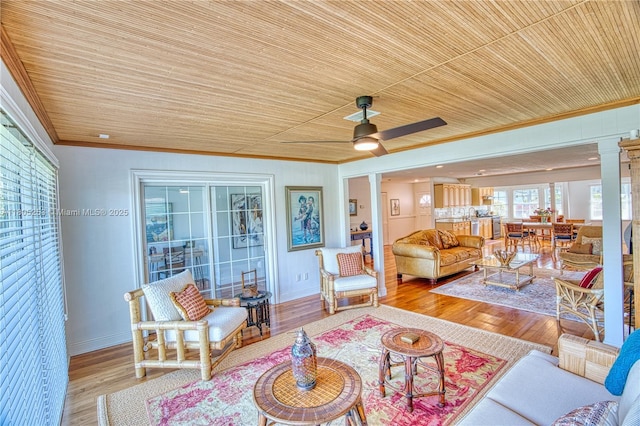 living area featuring wooden ceiling, ornamental molding, a ceiling fan, wood finished floors, and baseboards