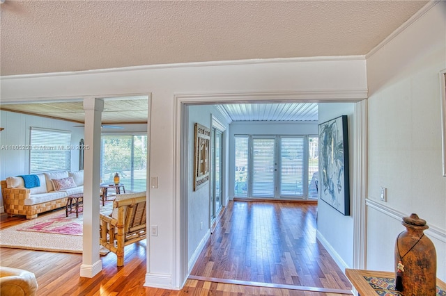 hallway featuring ornamental molding, wood finished floors, ornate columns, baseboards, and a textured ceiling
