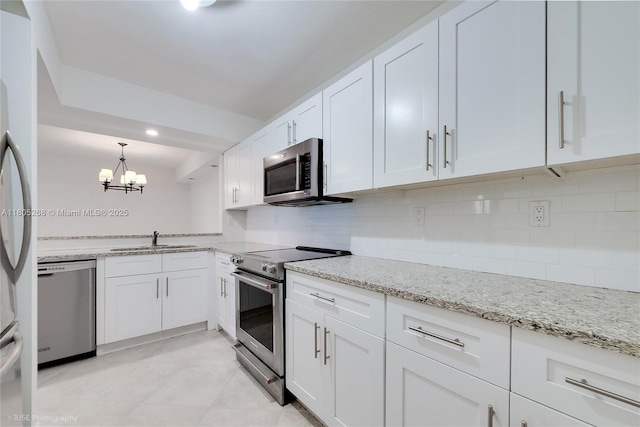 kitchen featuring appliances with stainless steel finishes, a sink, white cabinets, tasteful backsplash, and light stone countertops