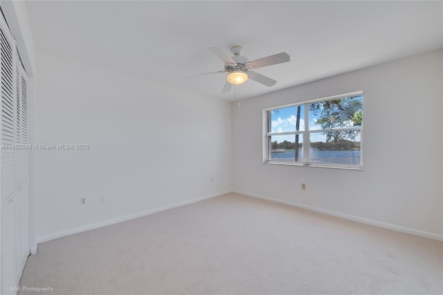 unfurnished room with light colored carpet, ceiling fan, baseboards, and a water view