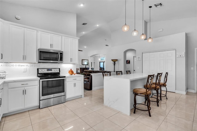 kitchen with stainless steel appliances, arched walkways, light tile patterned floors, white cabinetry, and high vaulted ceiling