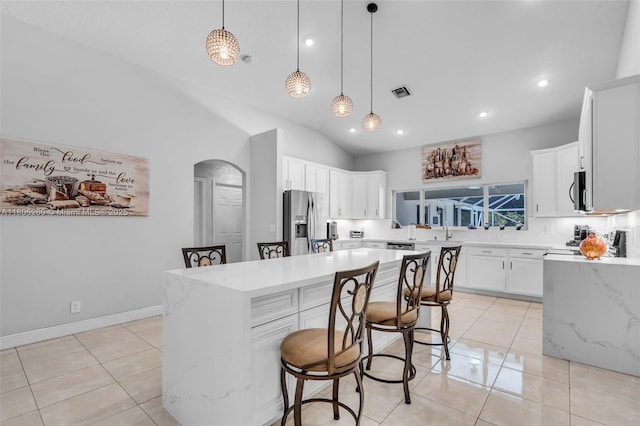 kitchen with appliances with stainless steel finishes, arched walkways, a sink, vaulted ceiling, and a center island