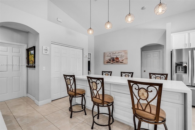 kitchen with arched walkways, stainless steel refrigerator with ice dispenser, a breakfast bar, light countertops, and light tile patterned floors