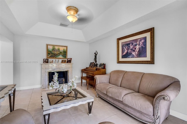 living area with a raised ceiling, ceiling fan, a premium fireplace, and tile patterned flooring