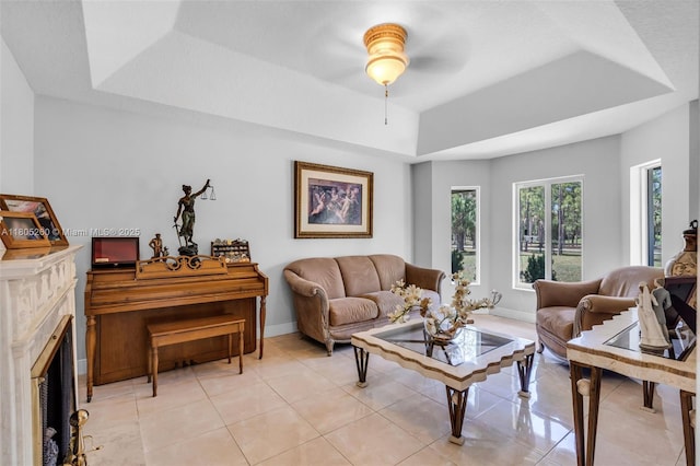 living area with a tray ceiling, light tile patterned floors, ceiling fan, a fireplace, and baseboards
