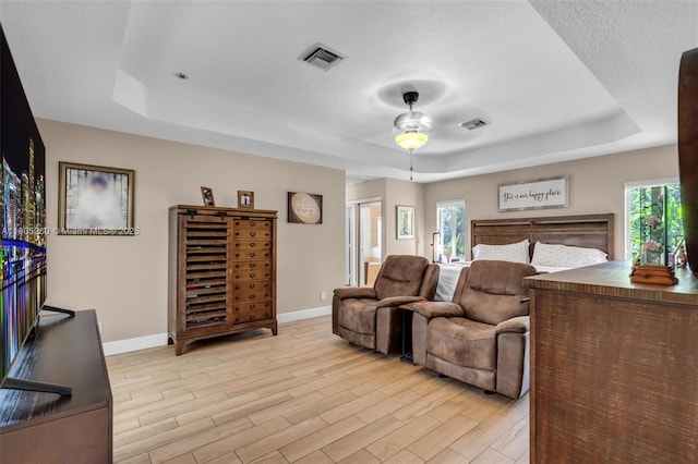 bedroom with a raised ceiling, baseboards, light wood-type flooring, and multiple windows