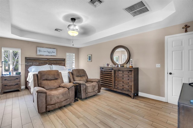 bedroom with a raised ceiling, light wood finished floors, baseboards, and a ceiling fan