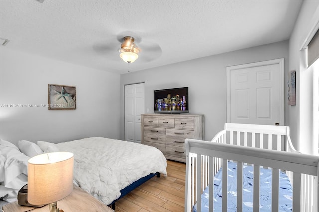 bedroom with light wood-type flooring, a textured ceiling, ceiling fan, and a closet