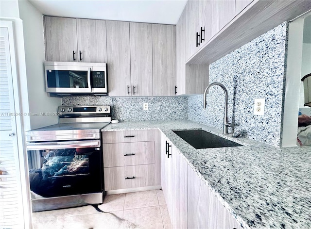 1701 NE 191st St Unit A108, Miami, FL 33179 - kitchen featuring stainless steel appliances, a sink, light stone counters, tasteful backsplash, and light tile patterned floors