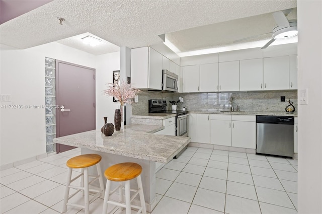 9341 Collins Ave Unit 1204, Surfside, FL 33154 - kitchen featuring appliances with stainless steel finishes, a sink, a peninsula, decorative backsplash, and light tile patterned floors
