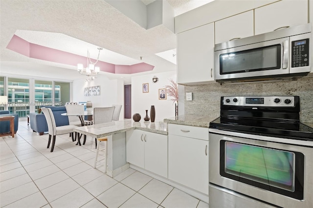 9341 Collins Ave Unit 1204, Surfside, FL 33154 - kitchen with stainless steel appliances, a peninsula, light tile patterned floors, white cabinets, and a chandelier