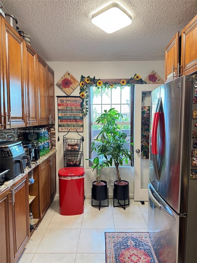 9481 W Elm Ln, Miramar, FL 33025 - kitchen featuring freestanding refrigerator, a textured ceiling, brown cabinetry, and light tile patterned floors