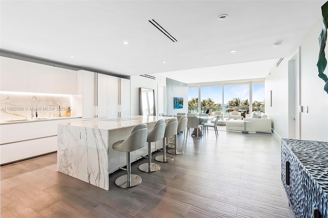 10203 Collins Ave Unit 302, Bal Harbour, FL 33154 - kitchen with light wood-style flooring, white cabinets, a kitchen bar, a sink, and recessed lighting