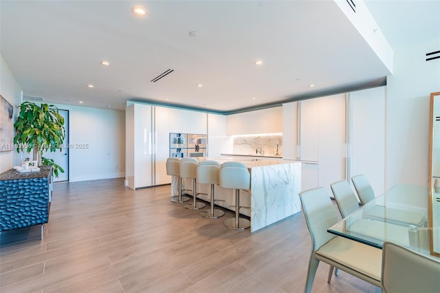 10203 Collins Ave Unit 302, Bal Harbour, FL 33154 - kitchen with white cabinetry, light wood-style flooring, recessed lighting, a center island, and decorative backsplash
