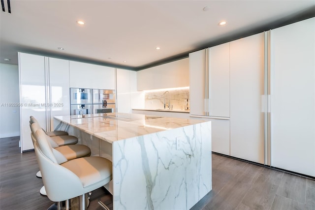 10203 Collins Ave Unit 302, Bal Harbour, FL 33154 - kitchen featuring modern cabinets, wood finished floors, white cabinetry, light stone countertops, and double oven