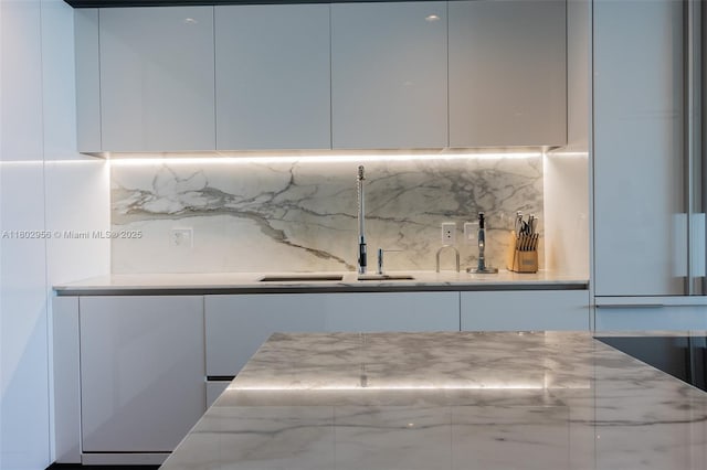 10203 Collins Ave Unit 302, Bal Harbour, FL 33154 - kitchen featuring modern cabinets, white cabinets, tasteful backsplash, a sink, and light stone counters