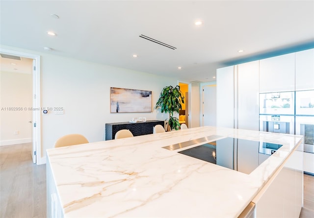 10203 Collins Ave Unit 302, Bal Harbour, FL 33154 - kitchen featuring light stone countertops, recessed lighting, light wood-type flooring, white cabinets, and an island with sink