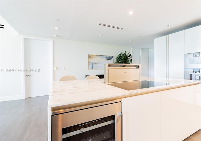 10203 Collins Ave Unit 302, Bal Harbour, FL 33154 - kitchen with wine cooler, light wood-style flooring, light stone counters, an island with sink, and white cabinetry