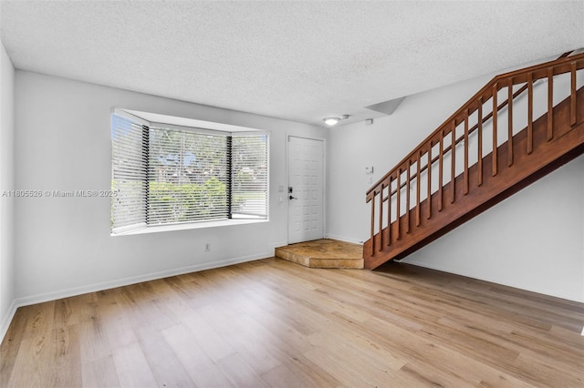 entrance foyer with wood finished floors, stairway, a textured ceiling, and baseboards