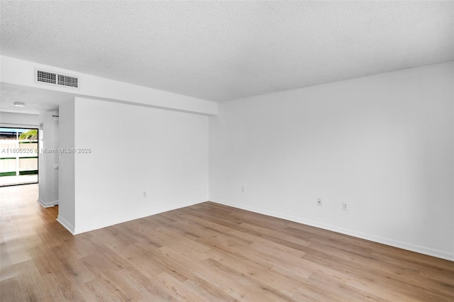 spare room with light wood-style flooring, baseboards, and a textured ceiling