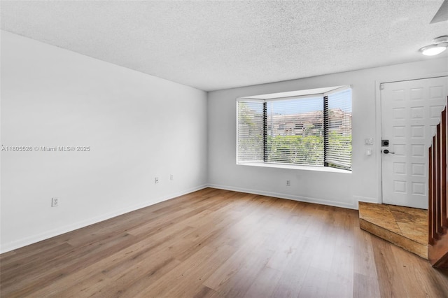 spare room featuring wood finished floors, a textured ceiling, and baseboards