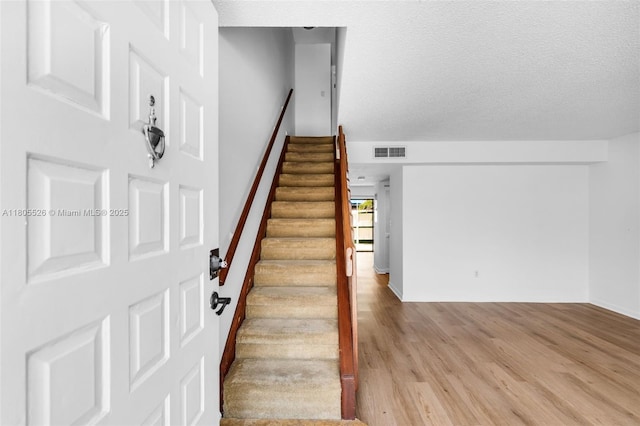 stairway with wood finished floors and a textured ceiling