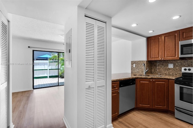 kitchen with appliances with stainless steel finishes, a sink, light wood-style floors, decorative backsplash, and dark stone counters