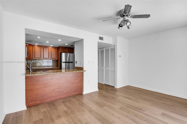 kitchen with freestanding refrigerator, a sink, light wood-style flooring, brown cabinets, and tasteful backsplash
