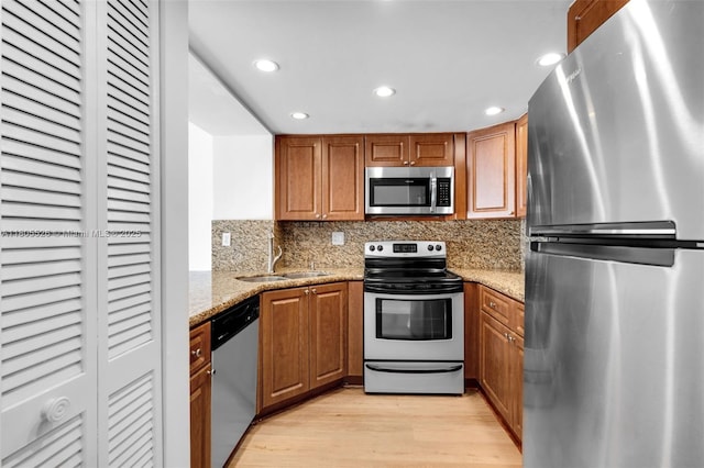 kitchen featuring appliances with stainless steel finishes, a sink, light wood-style flooring, recessed lighting, and light stone counters