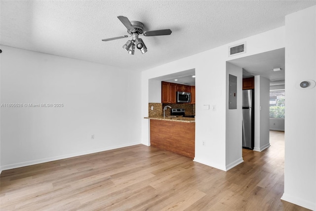 unfurnished living room featuring light wood finished floors, a ceiling fan, a textured ceiling, baseboards, and a sink