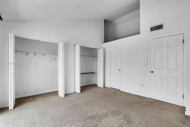 unfurnished bedroom featuring carpet, multiple closets, high vaulted ceiling, and a textured ceiling