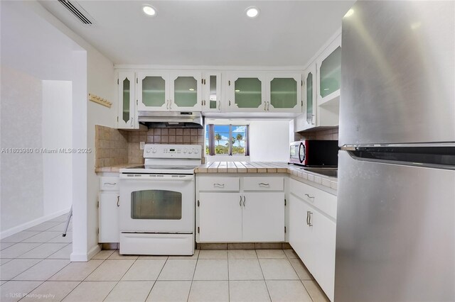 1551 NE Miami Gardens Dr Unit 322, Miami, FL 33179 - kitchen featuring appliances with stainless steel finishes, under cabinet range hood, backsplash, light tile patterned flooring, and white cabinetry