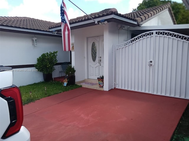 view of exterior entry featuring a tile roof, a gate, and stucco siding