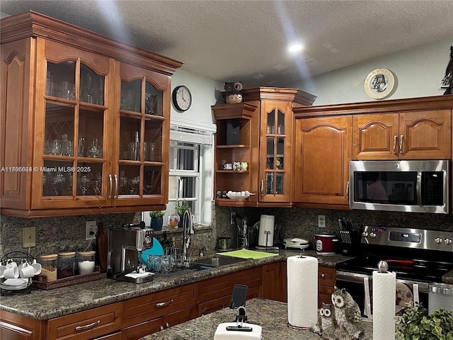 kitchen with stainless steel appliances, a sink, brown cabinetry, tasteful backsplash, and a textured ceiling