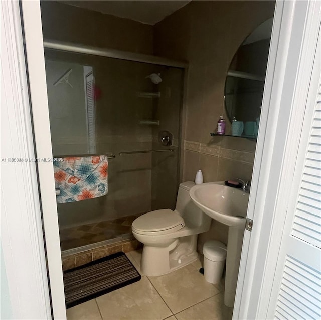full bath featuring tile patterned flooring, a stall shower, toilet, and tile walls