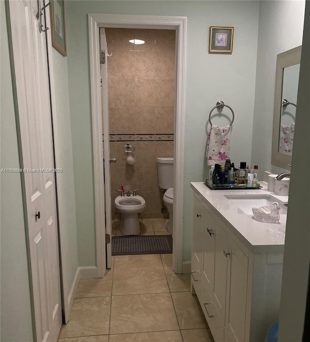 bathroom with tile patterned floors, toilet, a bidet, vanity, and tile walls