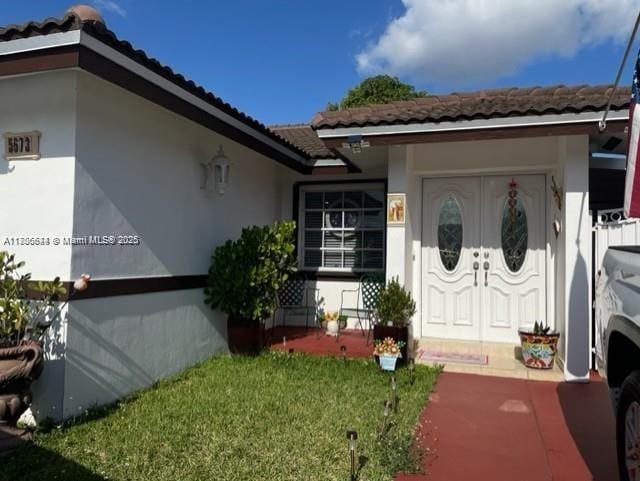 view of exterior entry featuring a tile roof, stucco siding, and a yard