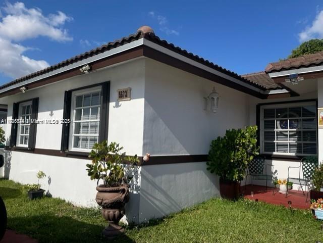 view of property exterior featuring stucco siding, a yard, and a tiled roof