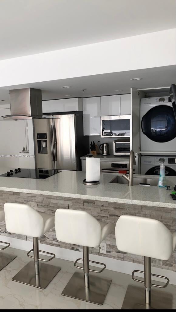 7601 E Treasure Dr Unit 1622, North Bay Village, FL 33141 - kitchen with stacked washer / drying machine, stainless steel appliances, a breakfast bar area, a sink, and white cabinetry