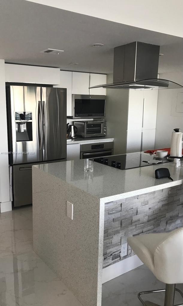 7601 E Treasure Dr Unit 1622, North Bay Village, FL 33141 - kitchen featuring stainless steel appliances, island range hood, modern cabinets, light stone countertops, and light marble finish floors