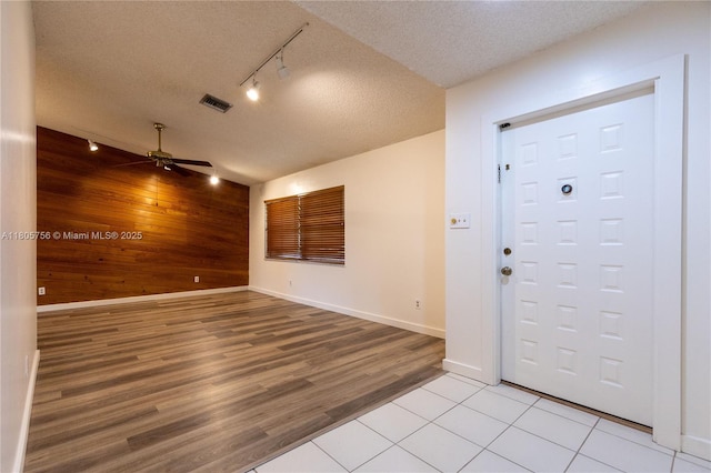 entrance foyer featuring rail lighting, wood walls, a ceiling fan, light wood finished floors, and a textured ceiling