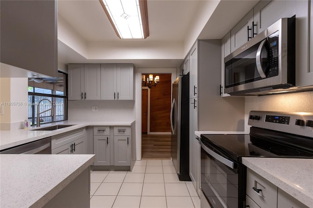 kitchen with appliances with stainless steel finishes, a sink, gray cabinetry, light countertops, and light tile patterned floors