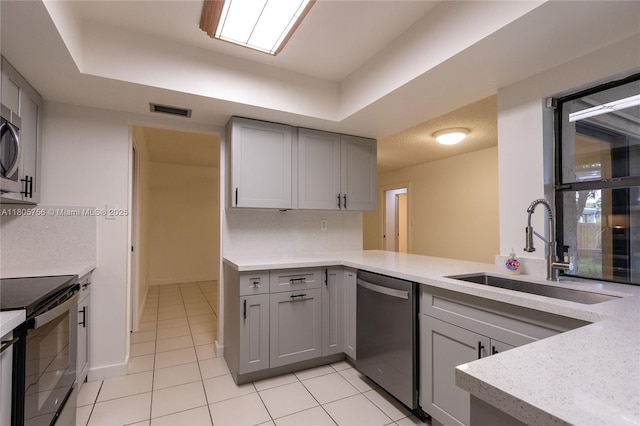 kitchen featuring stainless steel appliances, gray cabinetry, a sink, and a tray ceiling