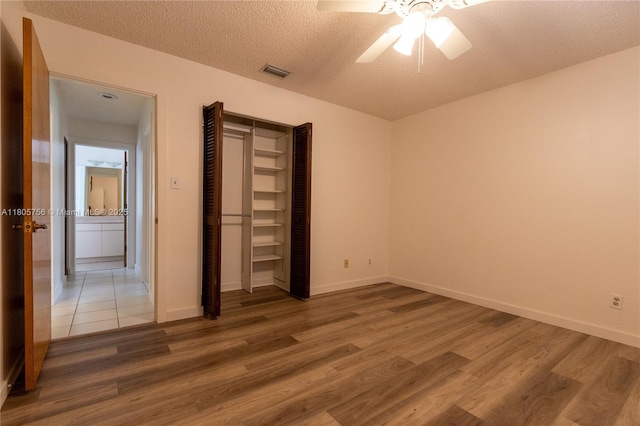 unfurnished bedroom with wood finished floors, baseboards, a textured ceiling, ceiling fan, and a closet