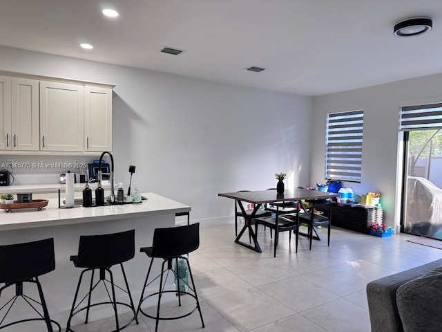 kitchen featuring light countertops, a breakfast bar area, light tile patterned floors, recessed lighting, and white cabinetry