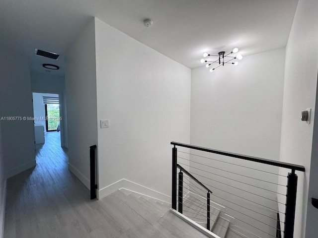 hall with an upstairs landing, wood finished floors, a chandelier, and baseboards