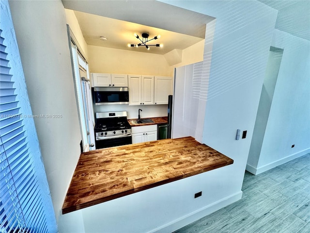 4710 Pine Tree Dr Unit 31, Miami Beach, FL 33140 - kitchen featuring appliances with stainless steel finishes, white cabinets, a sink, baseboards, and wood finished floors