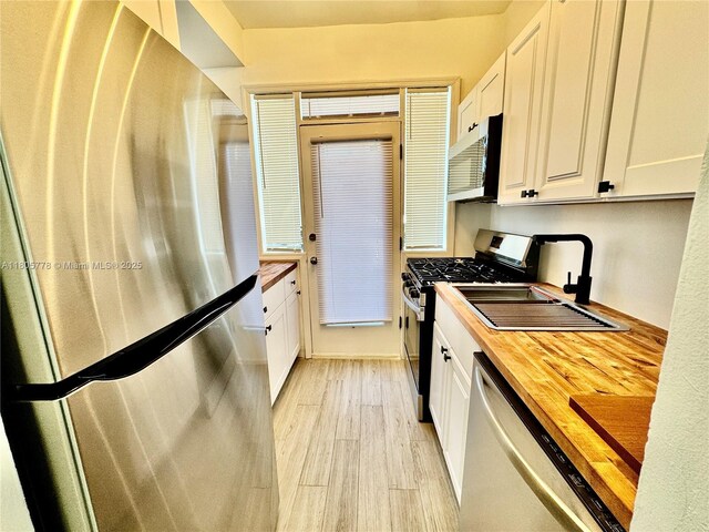 4710 Pine Tree Dr Unit 31, Miami Beach, FL 33140 - kitchen featuring appliances with stainless steel finishes, wood counters, white cabinets, and light wood-type flooring